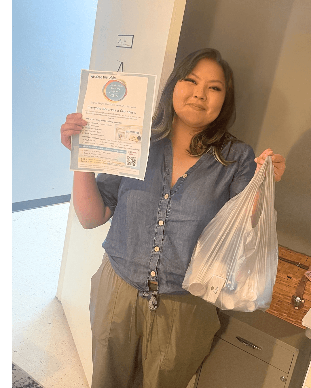Smiling woman holding a donation flyer and a plastic bag filled with hygiene products.